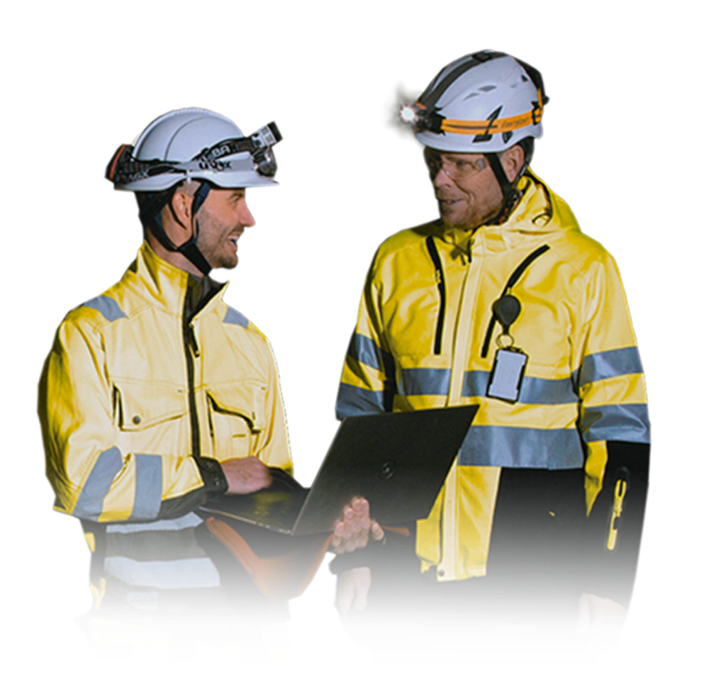 Mining professionals dressed in modern mining gear looking at a laptop screen together and smiling
